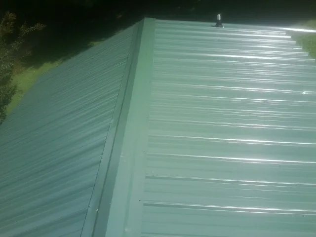 New green metal panels meeting at the ridge of a roof — Flat Roof Repair work by our crew in Bremen